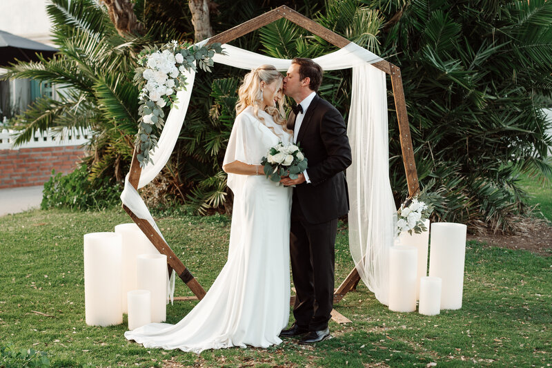 Wedding Photo Shoot Decor Inspo-Large Candles Framing a Bride and Groom Kiss at Wedding Arch